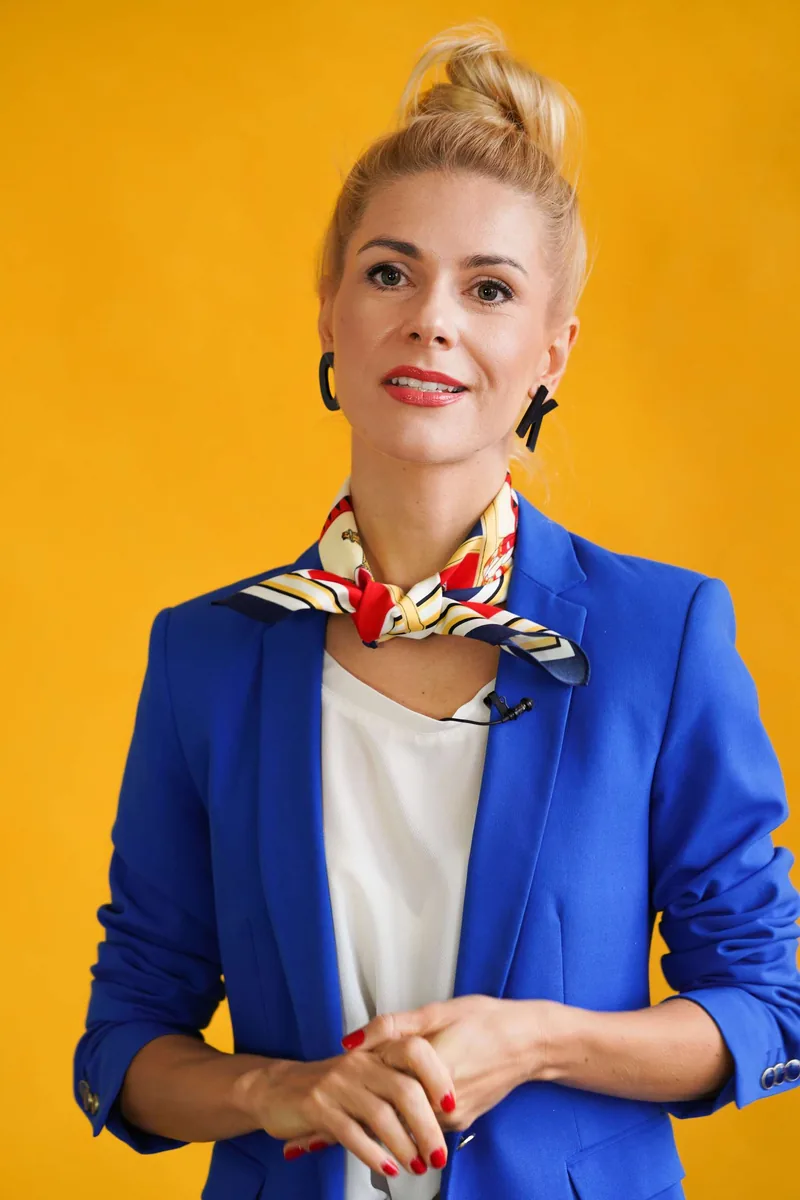 Olga Kairienė mėlynu švarku ir skarele, geltonas fonas