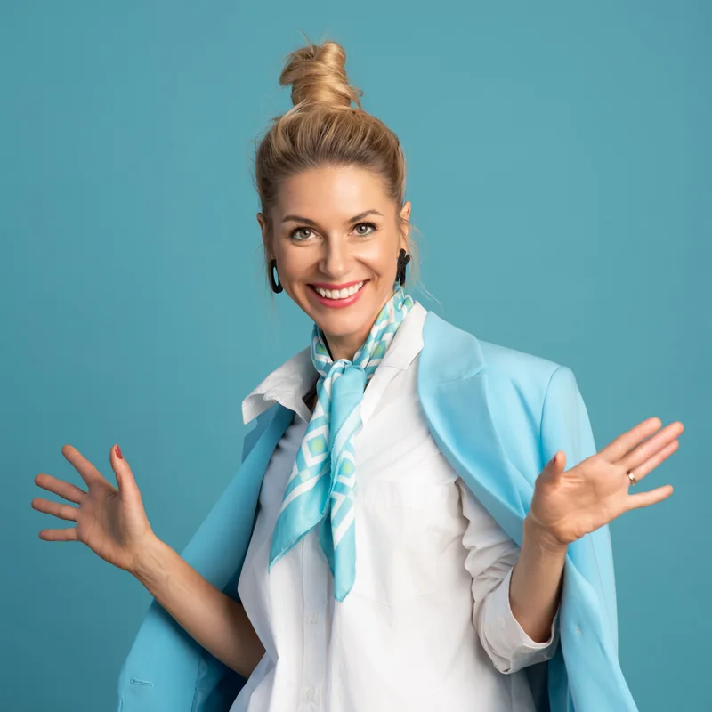 Olga Kairienė šypsosi, rankos atvertos, žydras fonas